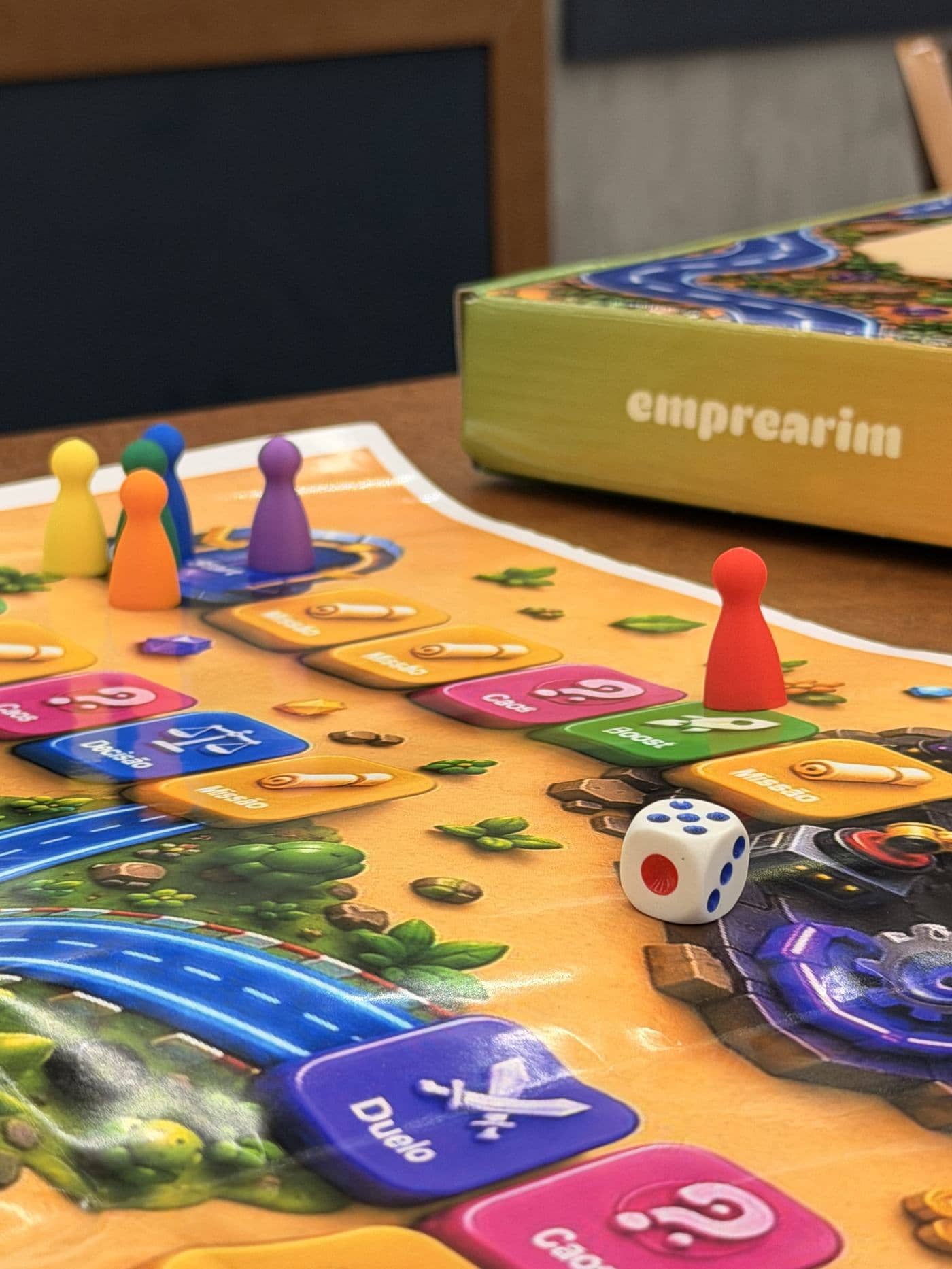 Tabuleiro do Emprearim com peões coloridos e dado sobre a mesa